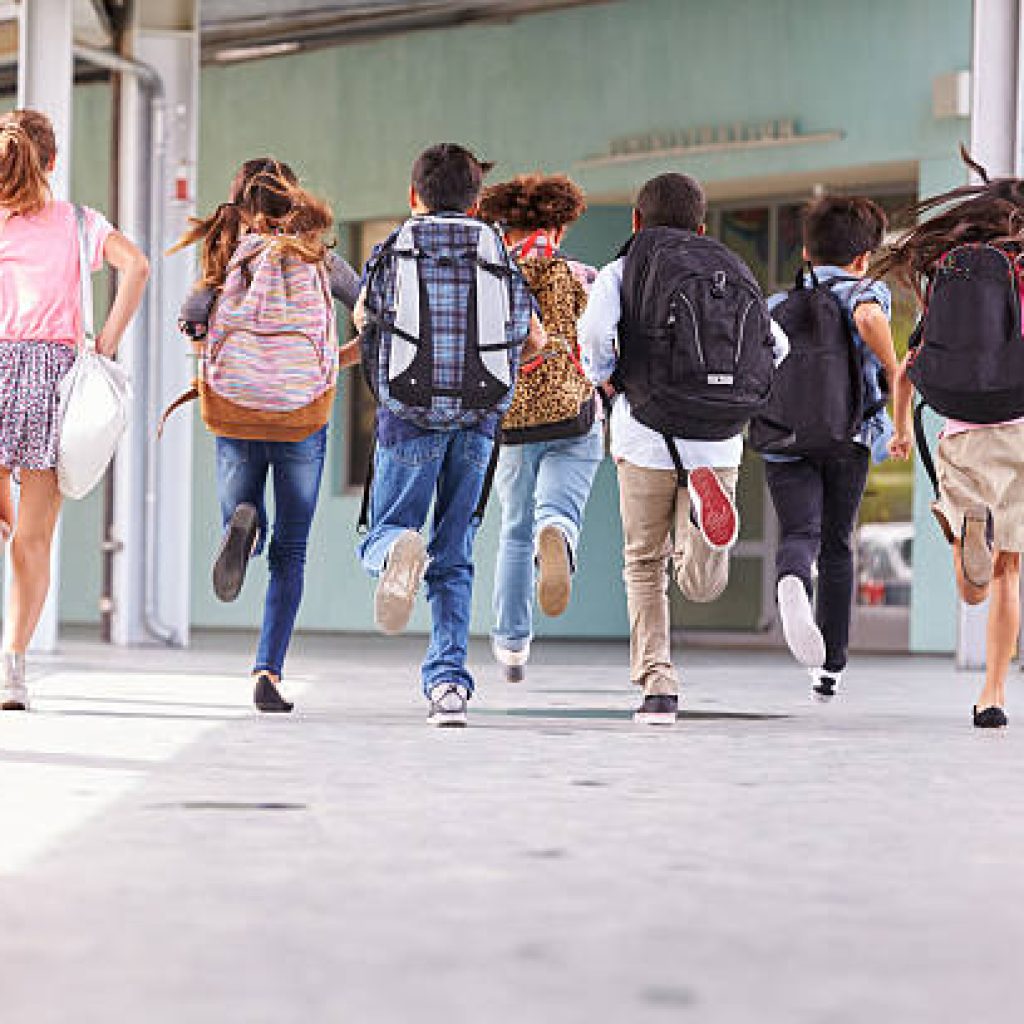 des élèves courent en portant leurs cartables dans la cour de l'école