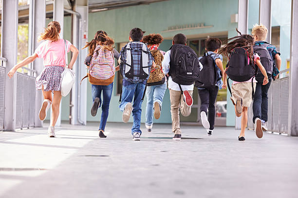 des élèves courent en portant leurs cartables dans la cour de l'école